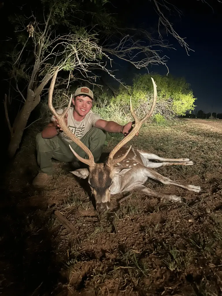 Brody Jackson holding a harvested fallow deer buck at night, highlighting successful guided hunting and field expertise.