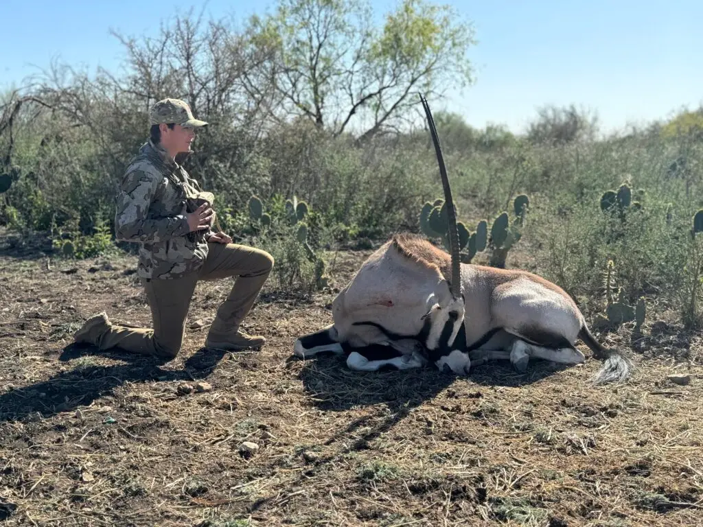 Brody Jackson kneeling beside a harvested scimitar-horned oryx during a guided exotic hunt in Texas, demonstrating field expertise and ethical wildlife management.